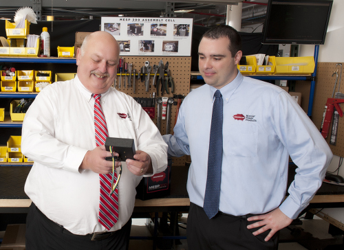 The image shows two men looking at an MESP controller. The man on the left is wearing a white shirt and red tie, and the man on the right is wearing a blue shirt and blue tie. 